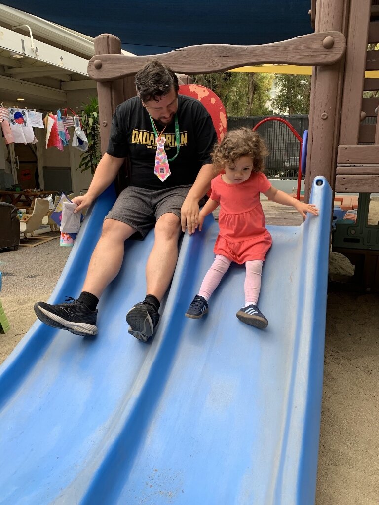 UPNS co-op parent and child sliding down the playground slide together during classroom workday
