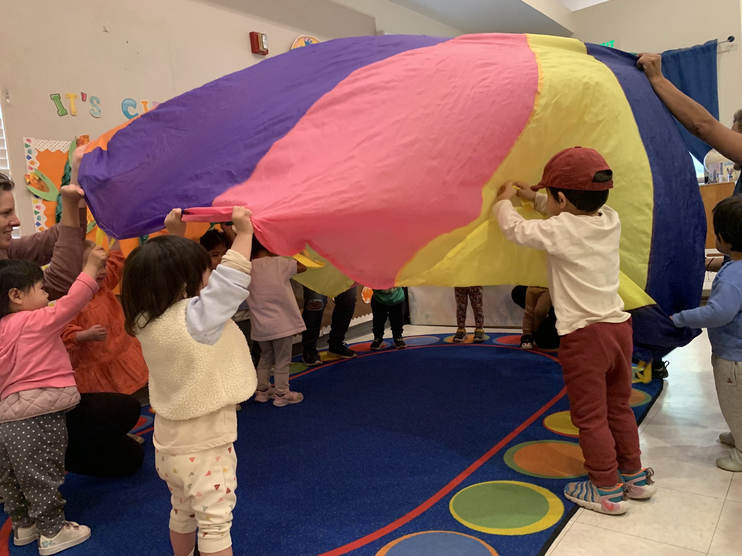 Children and teachers playing with the colorful rainbow parachute in the Kangaroo Room