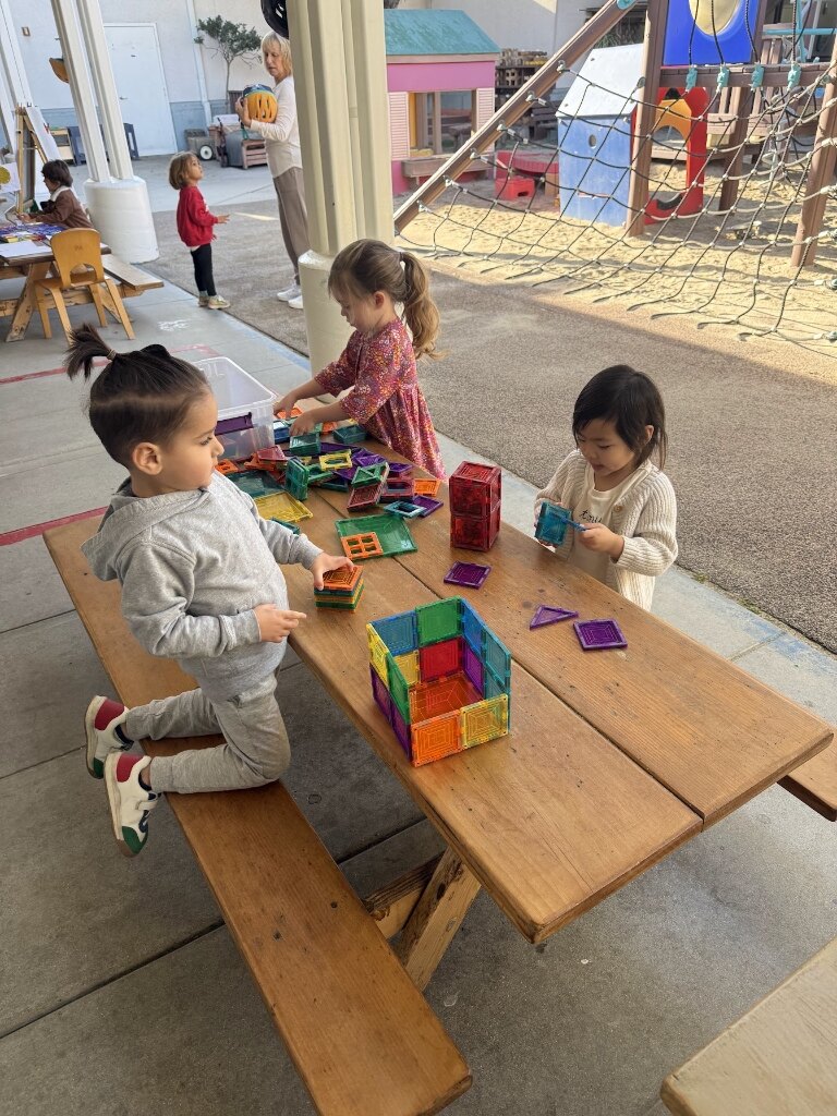 Children collaboratively building colorful magnetic structures at the outdoor picnic table